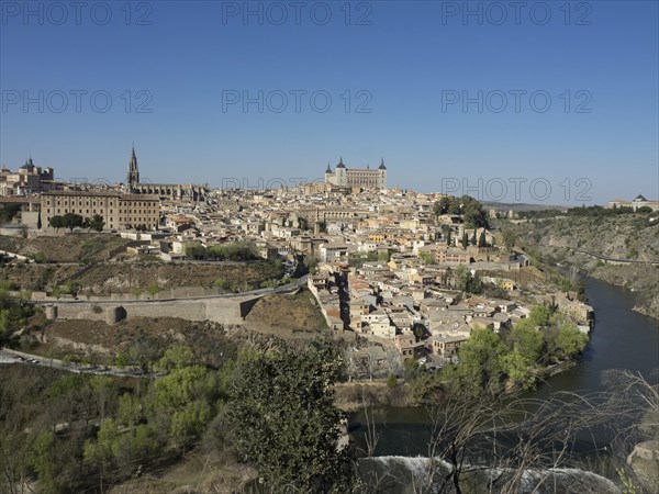 View of a historic riverside town with distinctive architecture and church towers, framed by hills