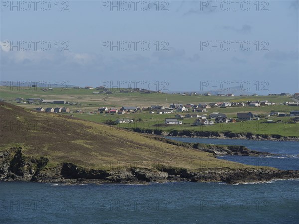 Green hills and houses of a village on a rocky coast with sea view, green meadows on a deep blue