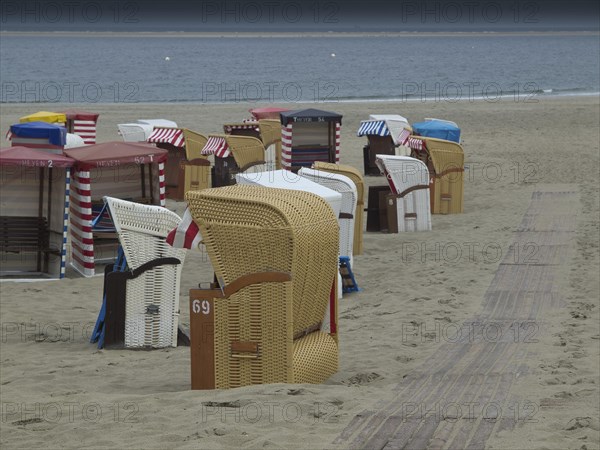 Several beach chairs standing on the sandy shore of a quiet beach with cloudy sky, beach chairs and