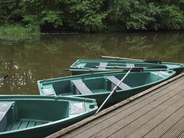 Green boats on a wooden jetty on a quiet river with trees in the background, green rowing boats on