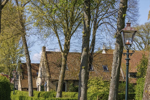 Red tiled houses and a lamppost, embedded in a green landscape with large trees, historic houses in