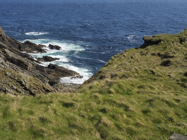 Rocky coast with green vegetation and a view of the blue sea, green meadows on a deep blue sea and