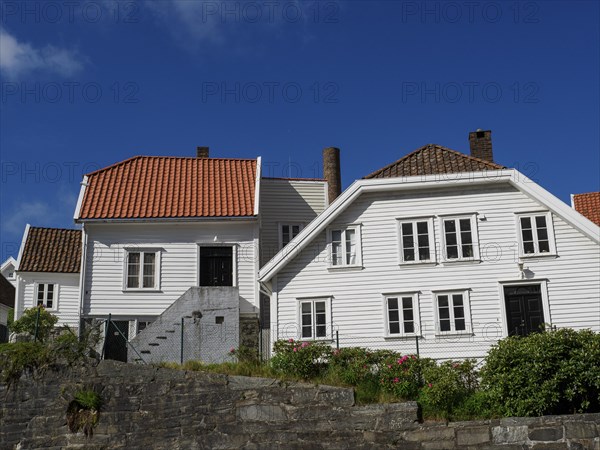 White wooden houses with tiled roofs and chimneys, stone wall in the foreground, sunny day, white