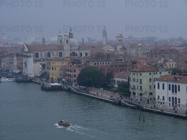 A foggy city view of Venice with historic buildings and boats on the canal, church towers and
