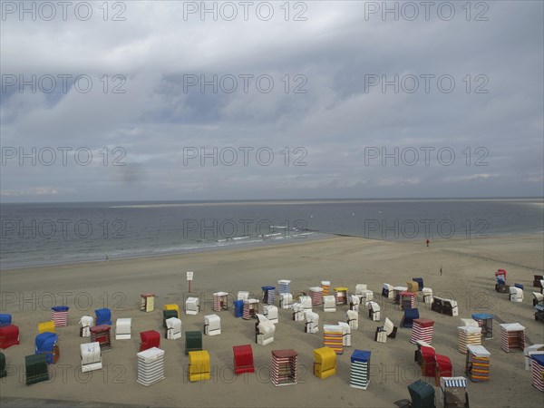 Colourful beach chairs stand abandoned on the beach while the sea and the clouds form the horizon,