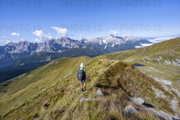 Mountaineers on a hiking trail between green mountain meadows on a mountain ridge, mountain
