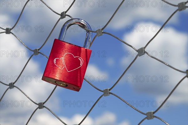 A single red love lock with two engraved hearts hangs from a bridge railing over the Danube,