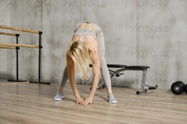 Middle-aged woman stretching back and arms in gym. Fitness athlete does bents and touching floor