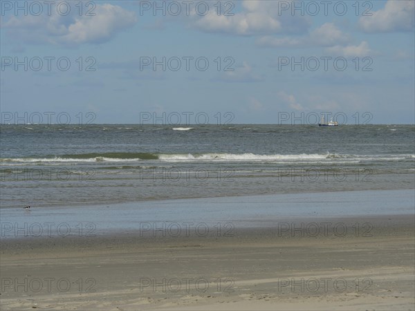 Seascape with a boat in the distance, gentle waves and wide sandy beach, beach and dunes with grass