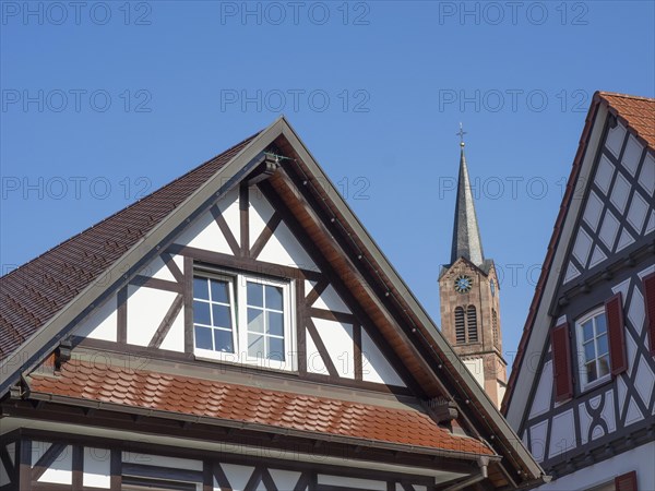 Detail of a half-timbered house with a view of a church tower under a bright blue sky, old