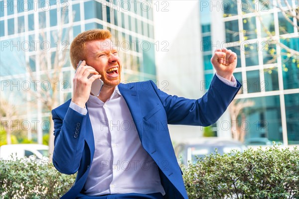 Businessman raising fist celebrating while talking to the mobile sitting in the city
