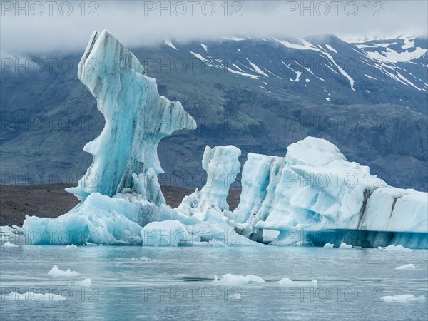 A majestic iceberg forms a breathtaking sculpture surrounded by water with mountains in the