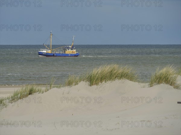 A fishing boat on the sea, surrounded by dunes and sand under a cloudy sky, dunes on an island with