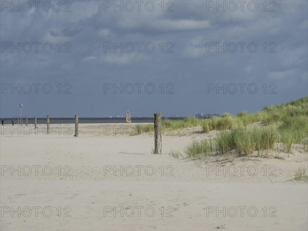 Sand dunes with tufts of grass and posts on the beach, distant windsurfers in the background,