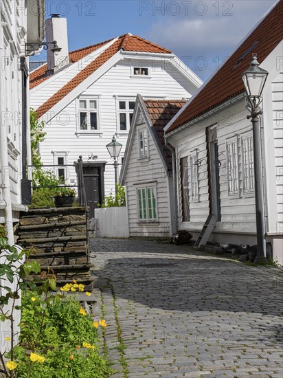 Cosy street with white wooden houses, flowers and a street lamp in sunny weather, white wooden