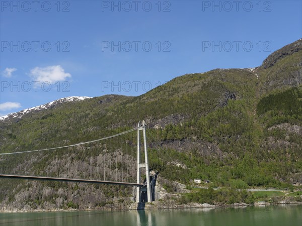Wide angle view of a bridge over green mountain slopes and forests under a clear blue sky, bridge