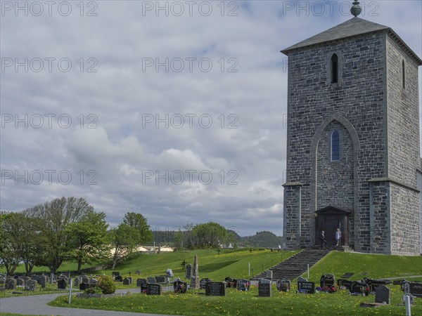 Stone church and cemetery with numerous gravestones under a cloudy sky in a rural setting, old