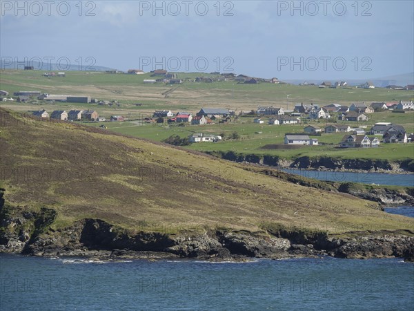 View of a coastal village with several houses on green fields, green meadows on a deep blue sea and