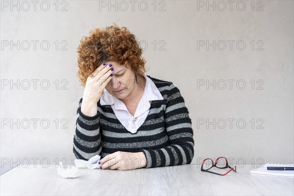 A mid-adult redhead woman is holding one hand on her forehead