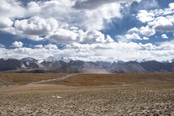 Car on a gravel track in the high mountain plateau, glaciated and snow-covered peaks, Ak Shyrak