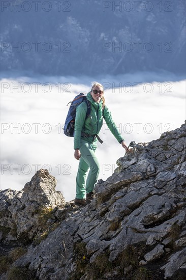 Hiker at Ettaler Manndl, view over mountain landscape and sea of clouds, high fog in the valley,