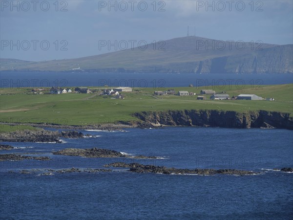 Coastal landscape with houses on green hills and blue ocean in the background, green meadows on a