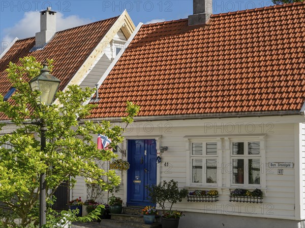 White house with red tiled roof and blue entrance, green plants and lantern in the foreground,