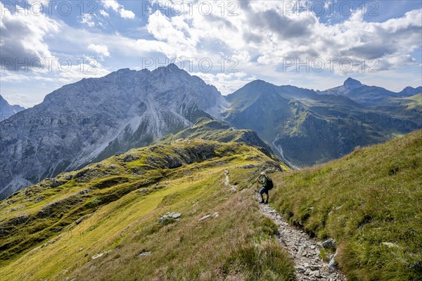 Mountaineer on a hiking trail on a grassy mountain ridge, idyllic mountain landscape with green