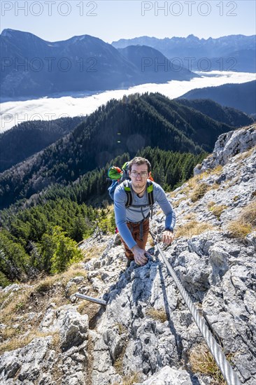 Hiker on via ferrata to Ettaler Manndl, view over mountain landscape and sea of clouds, high fog in