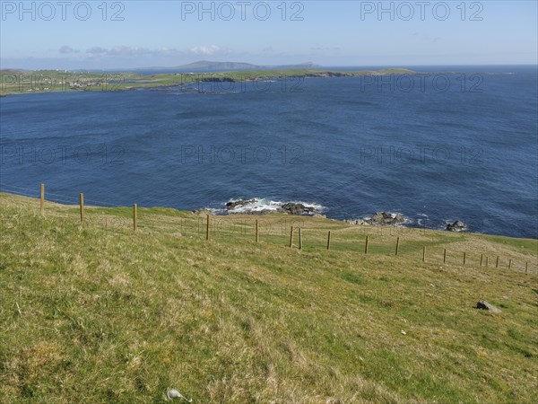 Green hills with a fence reaching to the blue sea, green meadows by a deep blue sea and a rocky