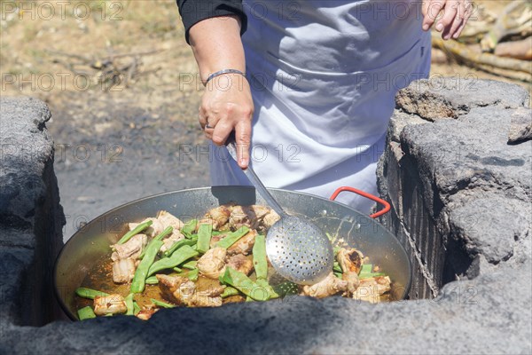 Closeup of a woman cook in a white apron preparing a typical Valencian paella on the fire in the