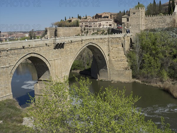 Stone bridge over a river with historic buildings and green vegetation in the background on a sunny
