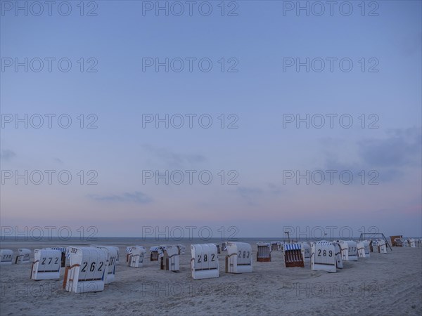A peaceful scene on the beach with white and striped beach chairs during dusk, setting sun on a