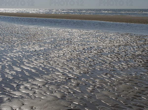 Beach with wavy sand surface and glittering water in front of a wide sea, glittering sea water at