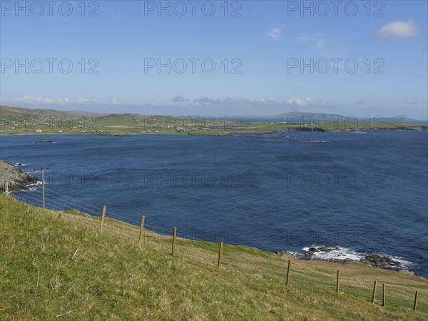 View of grassy plains and deep blue sea under a clear sky, green meadows by a deep blue sea and a