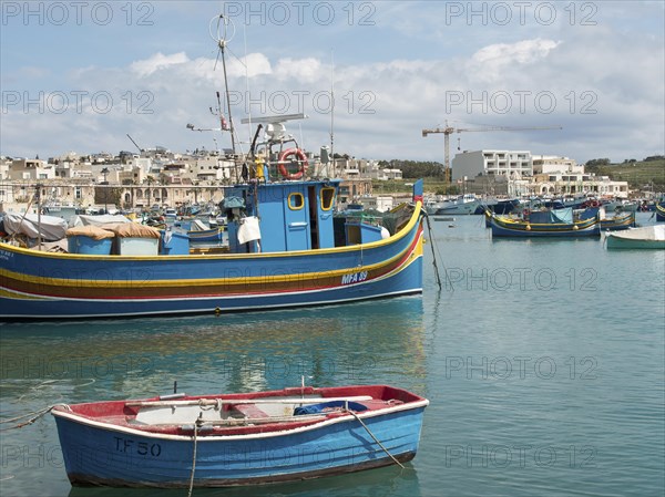 Harbour view with fishing boats and town in the background, a crane is visible, many colourful