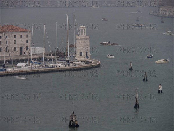 Venice harbour with numerous boats and yachts and a harbour wall in a foggy atmosphere, church