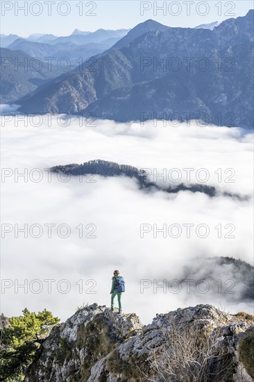 Hiker at Ettaler Manndl, view over mountain landscape and sea of clouds, high fog in the valley,