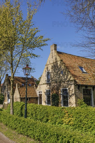 Cosy brick houses with red roofs, lampposts, green hedges and lush trees, historic houses in a
