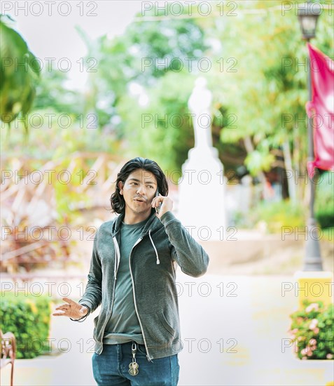 Young man gesturing and talking on the phone in a park. Latin guy talking on cell phone outdoors