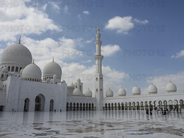 Mosque with a large courtyard, white domes and a high minaret under a slightly cloudy sky, large