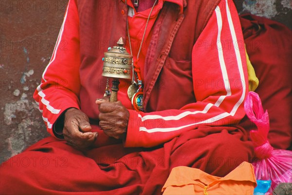A Tibetan monk in red robes holding a prayer wheel, immersed in spiritual practice