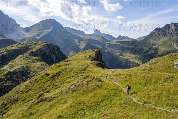 Mountaineer on a hiking trail on a grassy mountain ridge, idyllic mountain landscape with green
