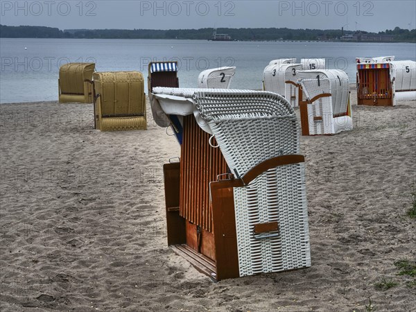 A quiet beach with several beach chairs and a stone quay in the background under a cloudy sky,