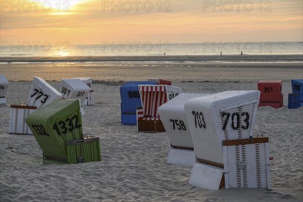 White, red and green beach chairs on a sandy beach at sunset, many colourful beach chairs on a warm