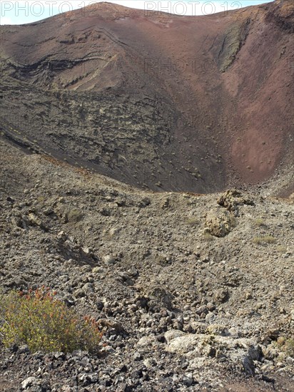 Close-up of a rocky crater with red volcanic soil and sparse vegetation, barren landscape with