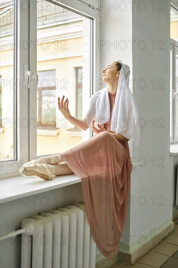 A ballerina sits on the windowsill during a break and repeats the movements of her hands