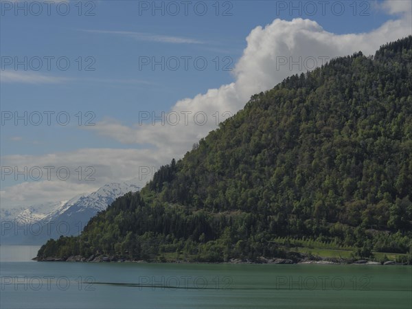Green mountains at a lake with partly cloudy sky, nature idyll, greenish shimmering water in a