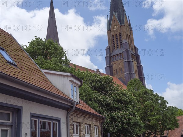 Church with high tower in a small village, surrounded by green trees and white clouds in the blue