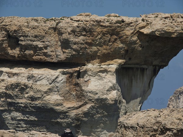 Large rock formation with natural erosion features under a blue sky, many historic windmills on a
